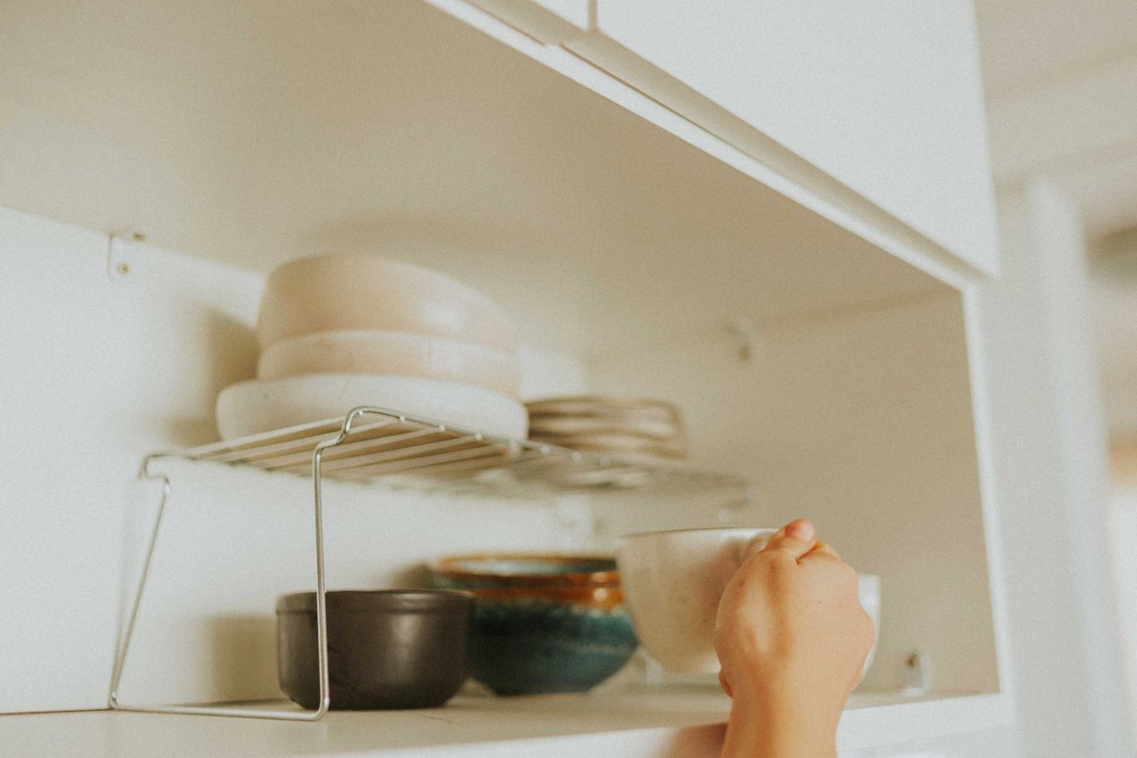 The Art of Drawing Readers In: Your attractive post title goes here A person reaches into a kitchen cabinet to grab a mug, surrounded by neatly stacked dishes.