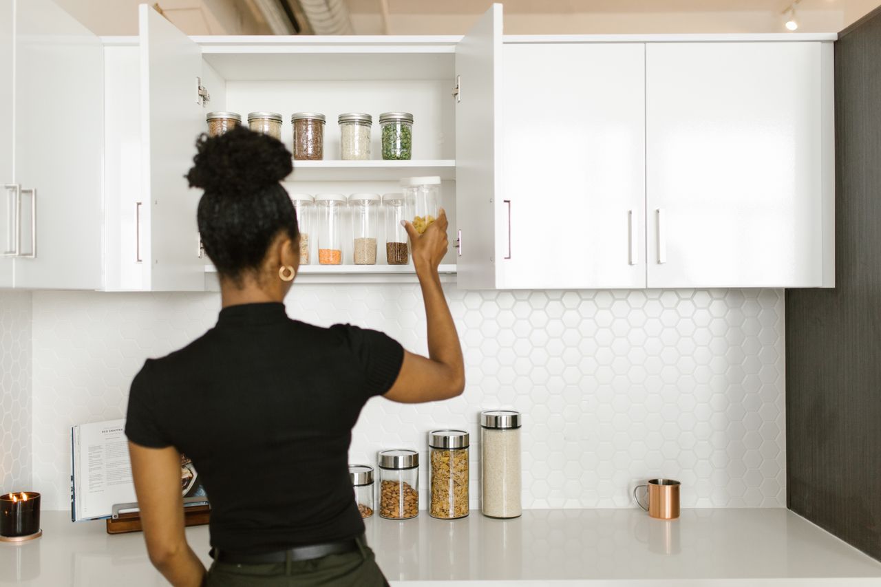 Mastering the First Impression: Your intriguing post title goes here A woman organizing a pantry shelf with various food jars in a modern kitchen.